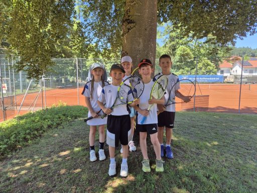 Kinder mit Tennisschlägern unter einem Baum vor dem Tennisplatz