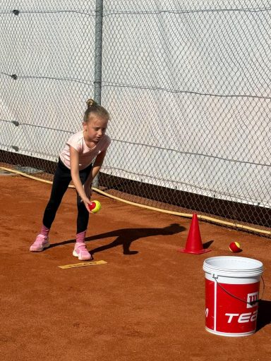 Mädchen wirft einen Tennisball in einen Eimer